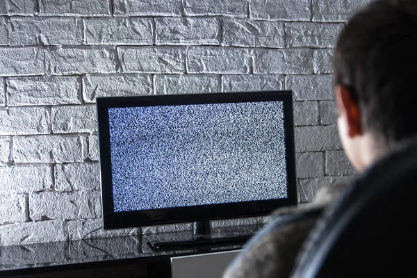 Menino assistindo TV lcd em um quarto escuro com paredes de tijolo estilo loft, vista traseira . — Fotografia de Stock