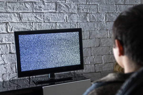 Menino assistindo TV lcd em um quarto escuro com paredes de tijolo estilo loft, vista traseira . — Fotografia de Stock