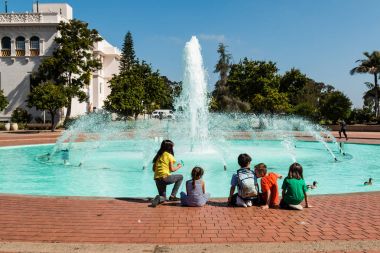 SAN DIEGO, CALIFORNIA - APRIL 28, 2017:  A group of children play near the Bea Evenson fountain, an iconic landmark located in Balboa Park, a popular urban cultural park.  clipart