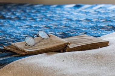 Antik gözlük bir yatakta yatarken bir yaşında kitap dinlenme.