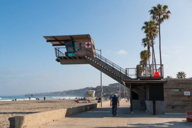 LA JOLLA, CALIFORNIA/USA - APRIL 28, 2018:  People walk on the boardwalk at La Jolla Shores Beach near the modern lifeguard station, which hovers over the beach to provide unobstructed staff views.   