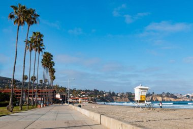 LA JOLLA, CALIFORNIA/USA - APRIL 28, 2018:  People walk along the beach and boardwalk at La Jolla Shores Park with La Jolla Cove in the background.