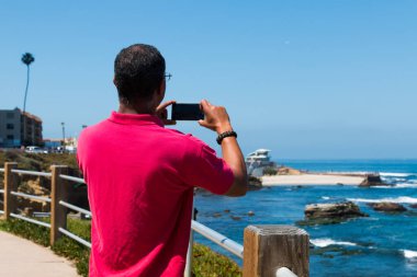 LA JOLLA, CALIFORNIA - JUNE 16, 2017:  A man takes a cell phone photograph of the historic Children's Pool and new modern lifeguard station.