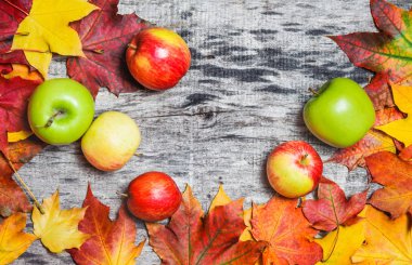 Sonbahar akçaağaç yaprakları ve elma ahşap tahta üzerinde dağınık