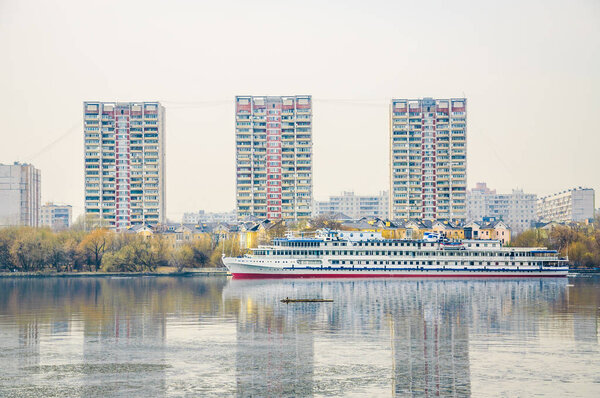 Three-deck ship at the pier Zakharkovo on the right bank of the Khimki reservoir. Three multi-storey apartment buildings and townhouses. Spring city landscape
