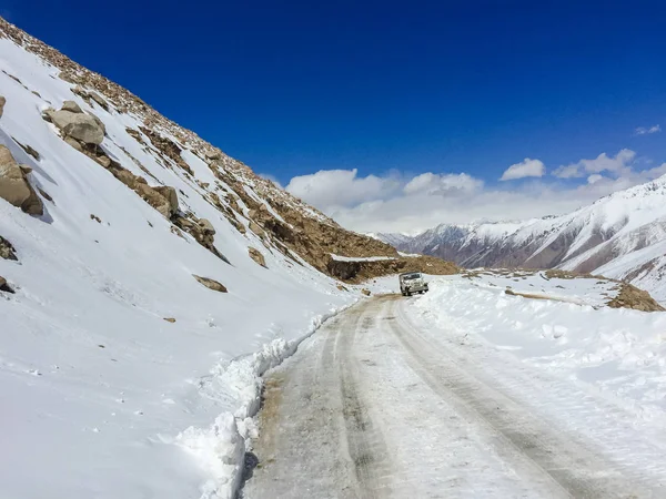 Vista panorâmica de inverno da estrada de asfalto nas montanhas cobertas de neve e árvores no lado da estrada em um fundo de céu azul e nuvens — Fotografia de Stock