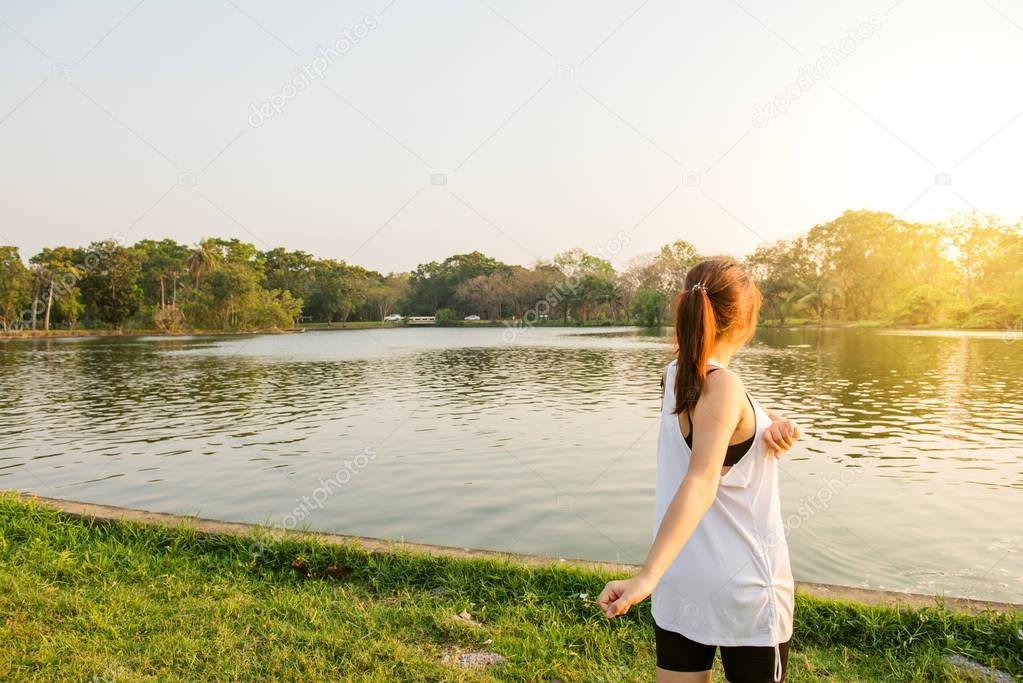 Happy successful sportswoman raising arms to the sky on golden back lighting sunset summer. Fitness athlete with arms up celebrating goals after sport exercising and working out outdoors. Copy space.