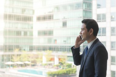 Aşağıda, şehirden bir ofis binası, cep telefonundan konuşurken en üst katında bir görünümünü büyük pencereden bakarak olgun ve kendinden emin iş çift arıyor