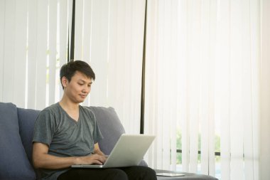 Evimde koltuk, rahatlatıcı, diz üstü bilgisayar ile oturma odasında oturup güzel genç adam gülümseyen.