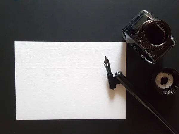 Sheet of paper, pen and ink of black on black office desk.