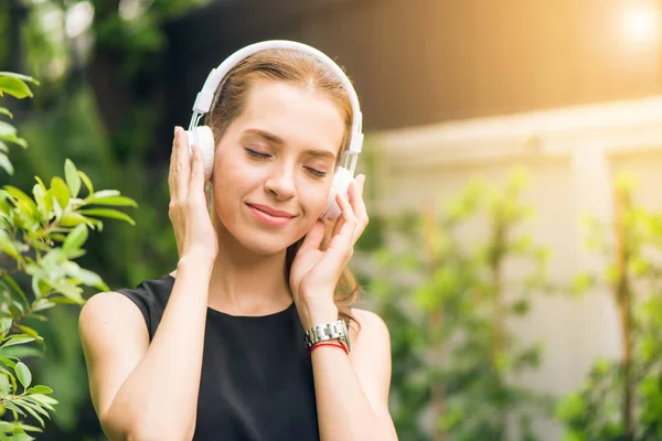 Gente concepto de ocio y tecnología - Mujer joven atractiva escuchando música en el reproductor de música al aire libre. Hipster chica disfrutando de las melodías en sus auriculares en el parque de la mañana. Lente llamarada . —  Fotos de Stock