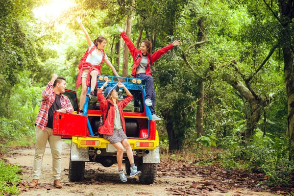 Glad asiatiska unga resenärer med 4wd bil av vägen i skogen, ungt par söker riktningar på kartan och en annan två njuter på 4wd bil. Ung blandad ras asiatisk kvinna och man. Stockbild