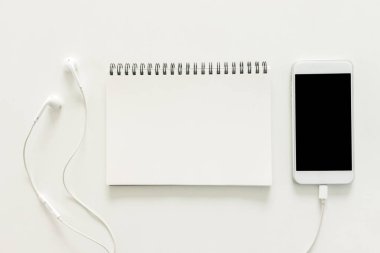 En az çalışma alanı - sketchbook ve hareket eden telefon ve kulaklık ile kopya alanı beyaz arka plan boş ekran fotoğraf çalışma masası yaratıcı düz yatırın. Üstten Görünüm, düz yatıyordu fotoğraf.