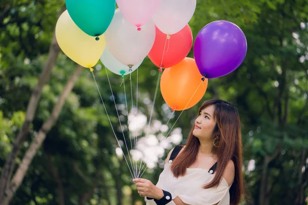 Lächelnde junge schöne asiatische Frauen mit langen braunen Haaren im Park. mit regenbogenfarbenen Luftballons in ihren Händen. Sonnige und positive Energie der Natur. — Stockfoto