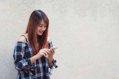 Gri arka plan üzerinde bir akıllı telefon kullanan mutlu güzel Asyalı kadın. Vintage etkisi tarzı resimler.