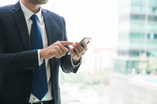 Empresario que usa mensajes de texto de aplicaciones de teléfonos móviles fuera de la oficina en la ciudad urbana con edificios de rascacielos en el fondo. Joven asiático hombre sosteniendo smartphone para trabajo de negocios . — Foto de Stock