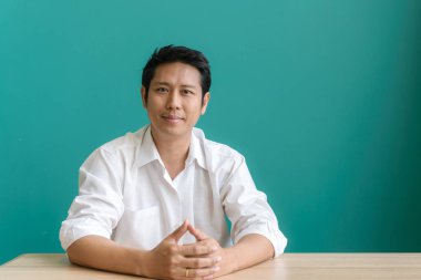 Zevk ile çalışma. Gülümseyen ve onun mavi duvar çalışma evinde otururken gülümseme ile kameraya bakarak Asya işadamı portresi. Vintage filtre uygulanmış görüntü.