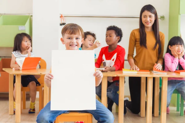 Leuke jongen houdt van lege witte poster met blij gezicht in de kleuter klas kleuterschool onderwijs concept, Vintage effect stijl foto 's. — Stockfoto