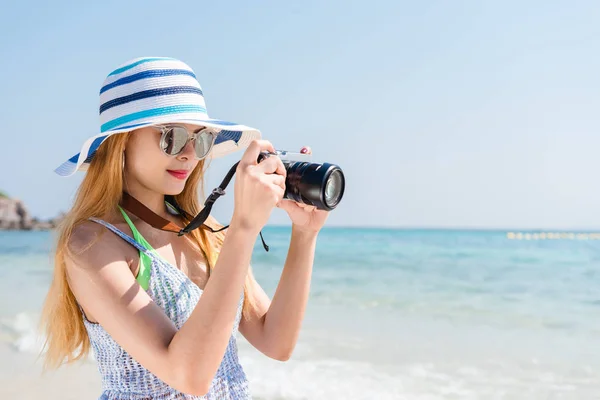 Feliz mulher asiática em férias fotografar com uma câmera na praia com o horizonte no fundo . — Fotografia de Stock