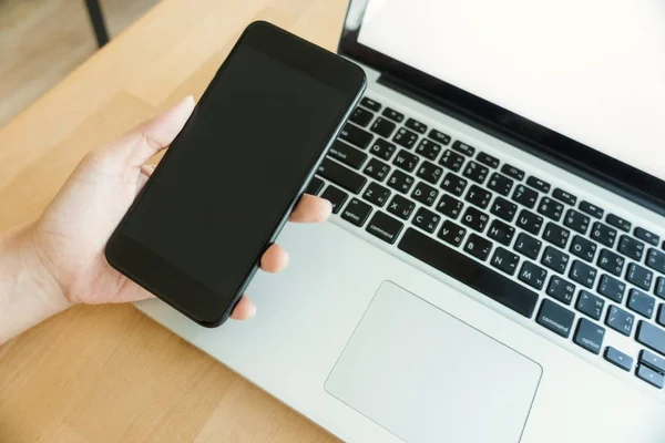 Jovem trabalhando em casa usando o mockup de telefone inteligente e computador portátil, as mãos do homem usando telefone inteligente no interior. Laptop e smartphone mockup. Fechar-se de homem segurando laptop e smartphone na mão . — Fotografia de Stock