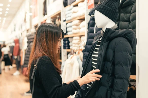 Halv kropp skott av en glad asiatisk ung kvinna med axelväska tittar på kläder hängande på järnväg inuti klädaffär. Shopping, mode, stil och människor kvinna koncept. — Stockfoto