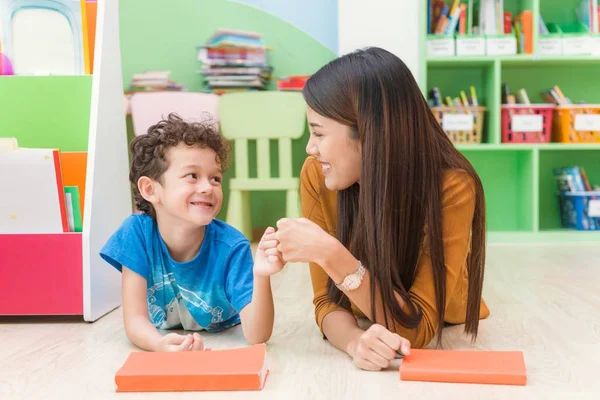 Young asian woman teacher teaching american kid in kindergarten classroom with happiness and relaxation. Education, elementary school, learning and people concept - teacher help school kids classroom. — Stock Photo, Image