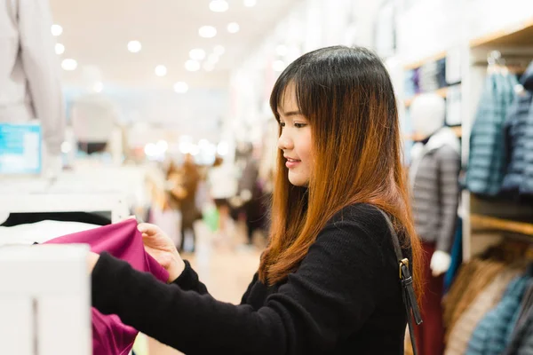 Halv kropp skott av en glad asiatisk ung kvinna med axelväska tittar på kläder hängande på järnväg inuti klädaffär. Shopping, mode, stil och människor kvinna koncept. — Stockfoto