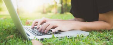 Genç Asyalı kadının bacakları açık dizüstü bilgisayar ile yeşil çimenlerin üzerinde. Kızın eller klavye. Mesafe öğrenme kavramı. Park içinde laptop üzerinde çalışan mutlu hipster genç Asyalı kadın. Panoramik afiş.