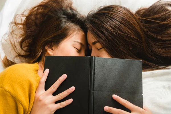 Top view of beautiful young asian women lesbian happy couple kiss and smiling while lying together in bed under book at home. Funny women after wake up. Lesbian couple together indoors concept. — Stock Photo, Image