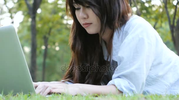 Les jambes de la jeune femme asiatique sur l'herbe verte avec ordinateur portable ouvert. Les mains de la fille sur le clavier. Concept d'enseignement à distance. Joyeux hipster jeune femme asiatique travaillant sur ordinateur portable dans le parc. Étudiant étudiant en plein air ; ordinateur portable ; étude ; femme ; blogueur ; parc ; fille ; printemps ; — Video