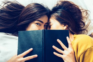 Üstten Görünüm güzel genç Asyalı kadınlar lezbiyen mutlu çift öpücük ve yan yana evinde kitabın altında yatakta yatarken süre gülümseyerek. Komik kadın uyan sonra. Lezbiyen çift birlikte kapalı kavramı.