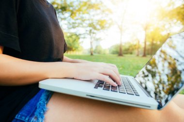 Genç Asyalı kadının bacakları açık dizüstü bilgisayar ile yeşil çimenlerin üzerinde. Kızın eller klavye. Mesafe öğrenme kavramı. Park içinde laptop üzerinde çalışan mutlu hipster genç Asyalı kadın. Öğrenci açık havada.
