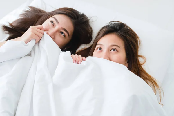 Top view of beautiful young asian women lesbian happy couple showing surprise and looking at camera while lying in bed under blanket. Funny women after wake up. Lesbian couple together indoors concept — Stock Photo, Image