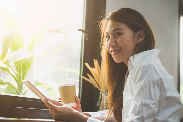 Jeune femme d'affaires en robe blanche assise à table dans un café et écrivant dans un cahier. Femme asiatique utilisant comprimé et tasse de café. Freelance travaillant dans un café. Apprentissage étudiant en ligne . — Photo