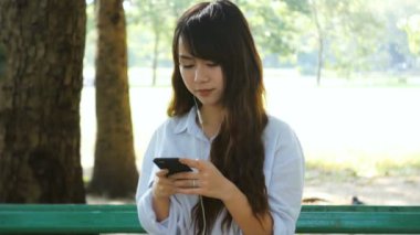 Sevimli kadın okuma hoş kısa mesaj cep telefonunda ılık bahar günü parkta otururken, muhteşem erkek kulaklık müzik dinlemek ve hücre telefon hakkında bilgi arama