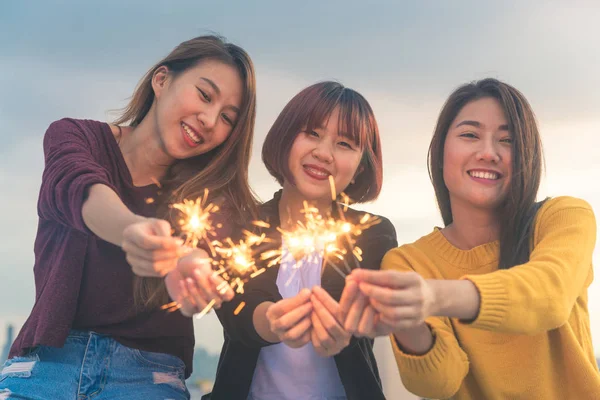 Outdoor shot of young people at rooftop party. Happy group of asia girl friends enjoy and play sparkler at roof top party at evening sunset. Holiday celebration festive party. Teenage lifestyle party.