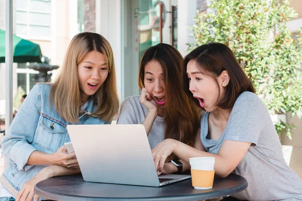 Grupo feliz asiático mujeres amigos viendo contenido multimedia en línea en el ordenador portátil sentado en la cafetería. Feliz asiáticas amigas dando regalo portátil a chica sorprendida en la cafetería. Compras concepto en línea . — Foto de Stock