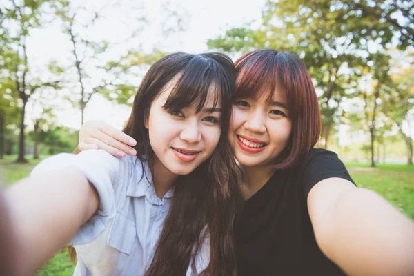 Deux belles jeunes femmes asiatiques heureuses amies s'amusent ensemble au parc et prennent un selfie. Joyeux hipster jeunes filles asiatiques souriant et regardant la caméra. Style de vie et concepts d'amitié . — Photo