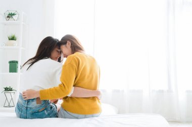 Back view of women lesbian happy couple waking up in morning, sitting on bed, stretching in cozy bedroom, looking through window. Funny women after wakeup. LGBT Lesbian couple together indoors concept clipart