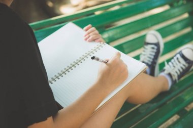 Mutlu hipster genç Asyalı kadın içine park günlüğüne yazma. Park içinde defter üzerinde mutlu hipster genç Asyalı kadın. Açık havada okuyan öğrenci. Yaşam tarzı kadın açık kavramı. Işık parlaması.