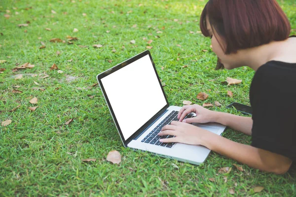 Imagem Mockup de uma mulher usando laptop com tela branca em branco deitado na grama no parque ao ar livre natureza. feliz hipster jovem asiático mulheres trabalhando no laptop no parque. Estilo de vida e conceitos de tecnologia . — Fotografia de Stock