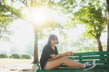 Mutlu hipster genç Asyalı kadın içine park günlüğüne yazma. Park içinde defter üzerinde mutlu hipster genç Asyalı kadın. Açık havada okuyan öğrenci. Yaşam tarzı kadın açık kavramı. Işık parlaması.
