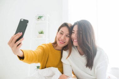 Yatak sarılmak üzerinde oturan ve evde selfie birlikte yatak odası alarak telefonu kullanarak güzel genç Asyalı kadınlar Lgbt lezbiyen mutlu çift. LGBT lezbiyen birlikte kapalı kavramı çift. Güzel vakit ev.