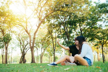 Parkta birlikte eğleniyor ve bir selfie alarak iki güzel mutlu genç Asyalı kadınlar arkadaş. Gülümseyen ve smartphone vasıl bakarak mutlu hipster genç Asyalı kızlar. Yaşam tarzı ve dostluk kavramları.