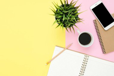 Ofis Masası adlı kullanıcının alanı - düz çalışma beyaz boş defter sayfası, kahve fincanı ve sahte telefon pastel arka plan üzerinde bir çalışma alanının en iyi görünümü yatırın. Pastel pembe sarı renk arka plan boşluk kavramı.