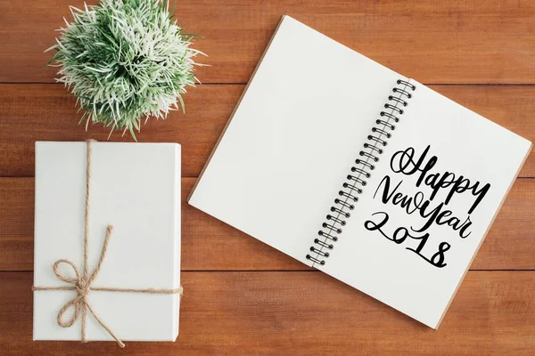 Wooden Work space - Flat lay view photo of working desk with happy new year wish notebook and a giftbox lying on brown wooden background. Top View flat lay photography. New year 2018 wishing concept