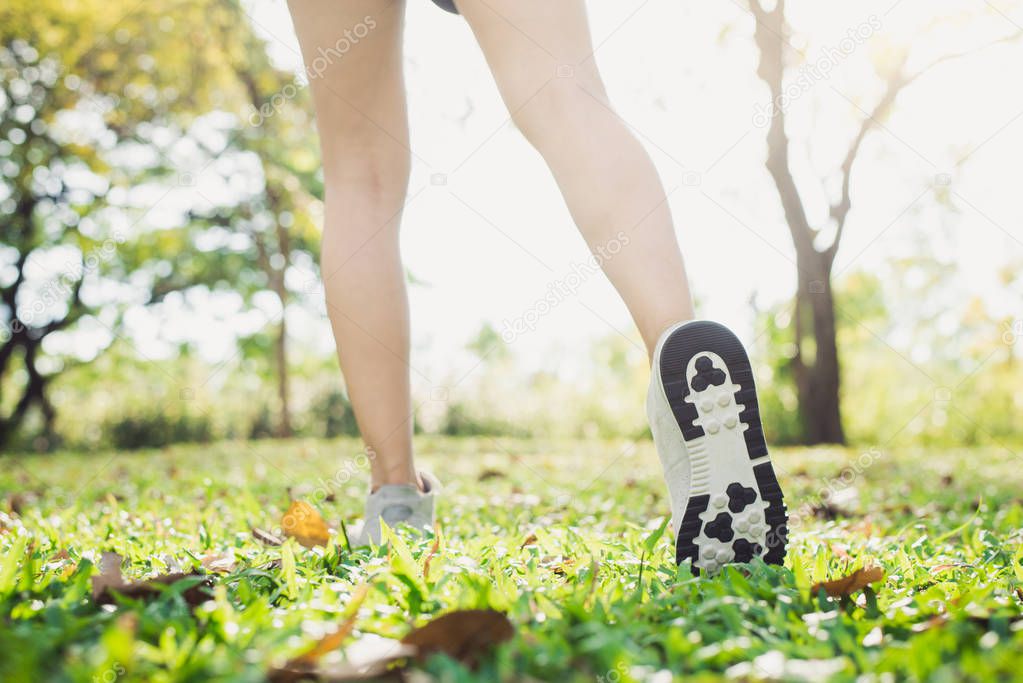 Close up of a young woman's legs in warming up the body by stretching her legs before morning excercise and yoga on the grass beneath warm light shining. Outdoor excercise concept.