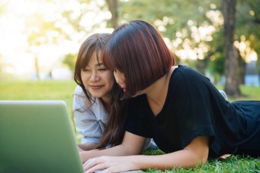 Çim üzerinde yalan ve dizüstü kullanarak ve yazarak genç Asyalı kadınlar. Kızlar eller klavye. Mesafe öğrenme kavramı. Park içinde laptop üzerinde mutlu hipster genç Asyalı kadınlar. Öğrenci açık havada.