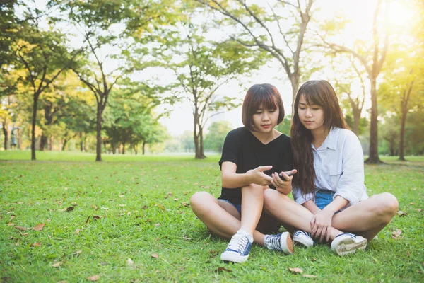 Dwóch przyjaciół piękny szczęśliwy młodych Azjatek, wspólna zabawa w parku i biorąc selfie. Szczęśliwy hipster młode Azjatki uśmiechając się i patrząc na smartfonie. Pojęcia dotyczące stylu życia i przyjaźni. — Zdjęcie stockowe