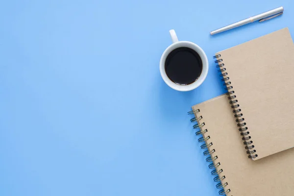 Office desk working space - Flat lay top view mockup photo of a working space with cup of coffee, notebooks and decoration on blue pastel background. Pastel blue color copy space working desk concept.